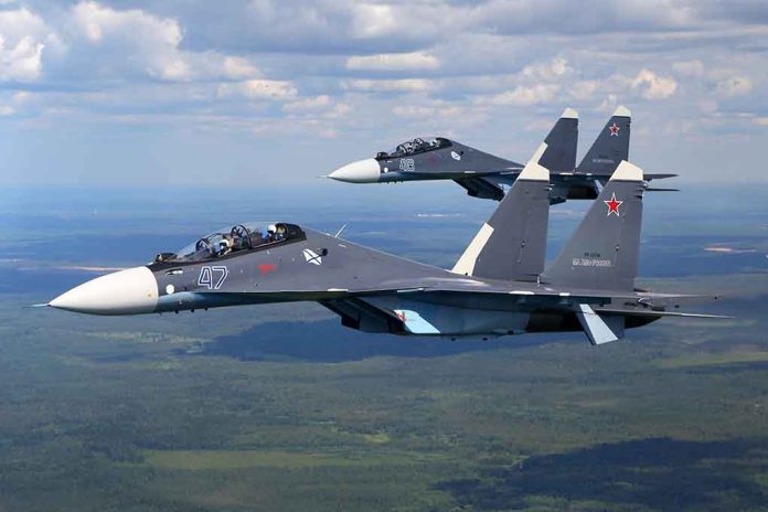 Two fighter jets flying in formation over green landscape.