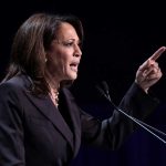Person speaking at podium with raised finger.