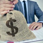 Bag with a dollar sign on it held by a man in a suit