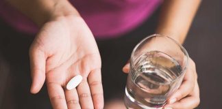 Woman holding a pill and a glass of water