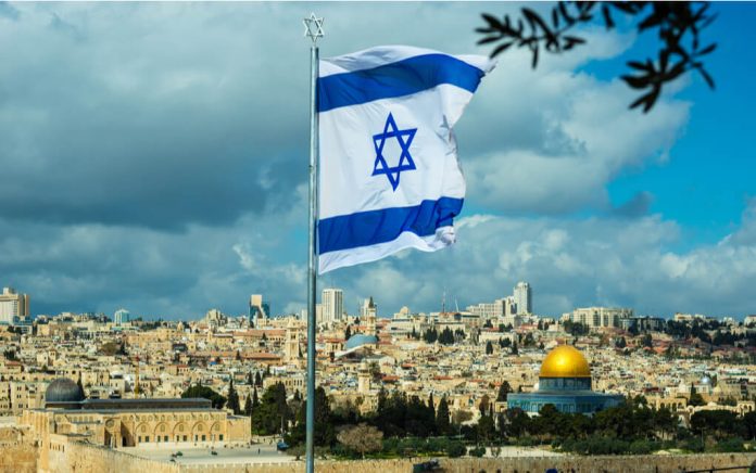 Israeli flag flying over Jerusalem cityscape and Dome.