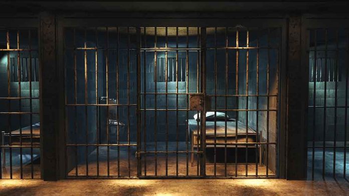 Empty prison cell with metal bars and bed.