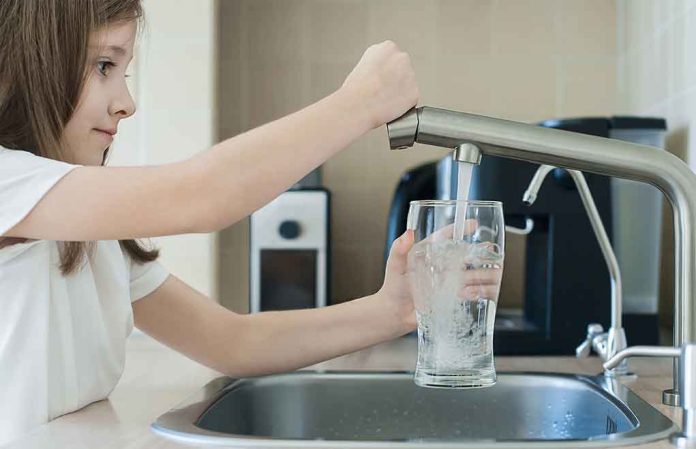 Girl filling glass with water from kitchen faucet.