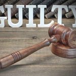 Judge's gavel and guilty sign on wooden table