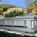 Silver casket with flowers at outdoor funeral.