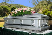 Silver casket with flowers at outdoor funeral.