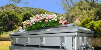 Silver casket with flowers at outdoor funeral.