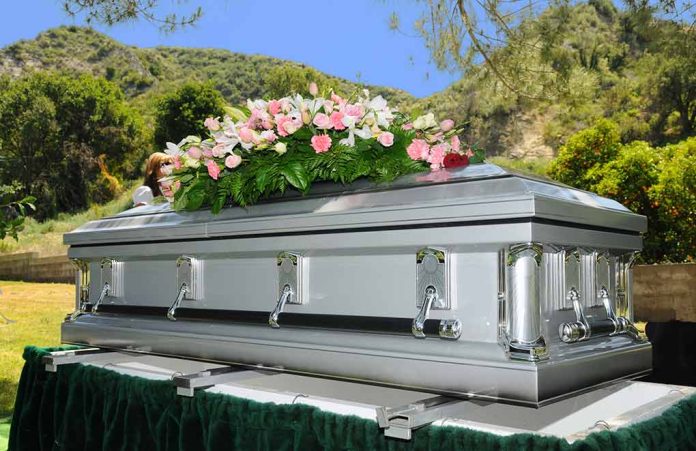 11952262 featured image Silver casket with flowers at outdoor funeral.