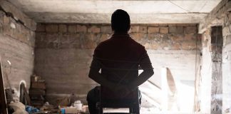 Person tied to chair in a dimly lit room