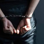 Hands in handcuffs behind back in dark room.