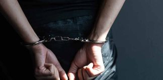 Hands in handcuffs behind back in dark room.