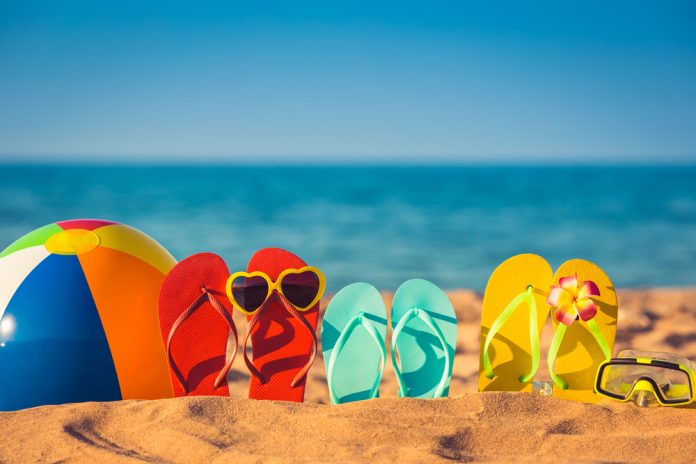 277455644 featured image Colorful beach ball flip flops sand sea background