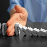 Hand stopping falling row of dominoes.