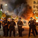 Police officers in riot gear near burning car