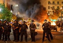 Police officers in riot gear near burning car