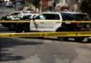Police tape blocking street with patrol cars