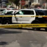Police tape blocking street with patrol cars