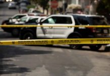 Police tape blocking street with patrol cars