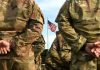 Soldiers stand in formation with American flag in background