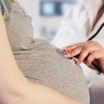 Doctor uses stethoscope on pregnant womans belly