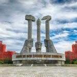 Concrete monument with hands holding tools under cloudy sky