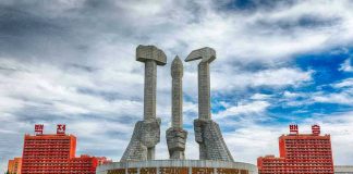 Concrete monument with hands holding tools under cloudy sky