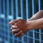 Close up of clasped hands resting on a blue fence