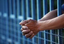 Close up of clasped hands resting on a blue fence
