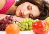 A woman resting her head on a table surrounded by various fruits