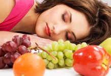 A woman resting her head on a table surrounded by various fruits
