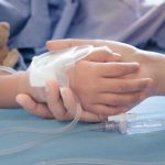 Childs hand with IV, held by adult.