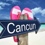 Cancun sign on a beach with flip-flops.
