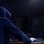 Hooded figure using dual monitors in dark room