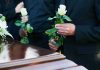 Mourners holding white roses by a casket