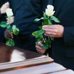 Mourners holding white roses by a casket