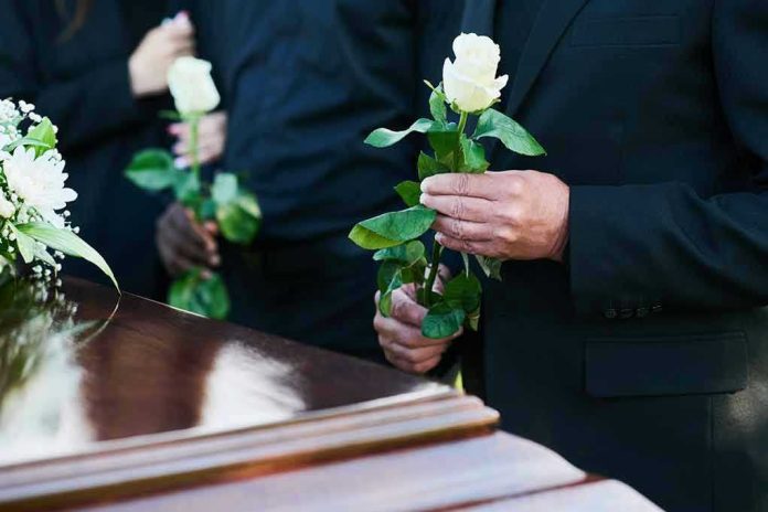 Mourners holding white roses by a casket