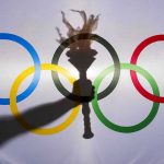 Shadow of torch over Olympic rings logo.