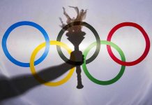 Shadow of torch over Olympic rings logo.