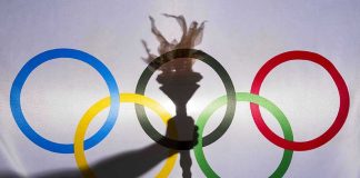 Shadow of torch over Olympic rings logo.