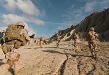 Soldiers running on rocky terrain with backpacks.