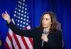 Woman speaking and gesturing with American flag background.