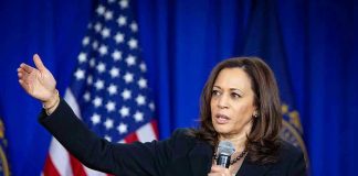 Woman speaking and gesturing with American flag background.