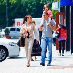 A family walking on a sidewalk in an urban area, with a child on the fathers shoulders