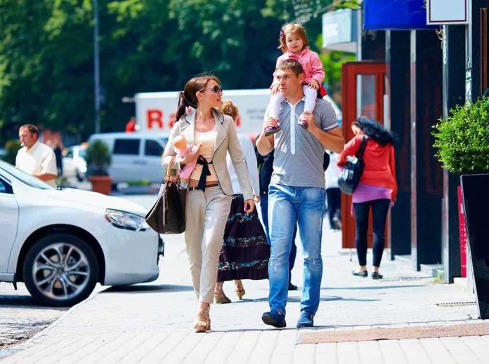 A family walking on a sidewalk in an urban area, with a child on the fathers shoulders