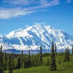 Trump’s Unleashes Alaska Mining Blitz Snow-covered mountain under blue sky with green foreground.