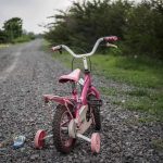 Pink childrens bike with training wheels on gravel path.