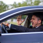 Man yelling inside a car, looking frustrated.