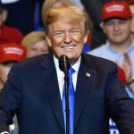 GOP Bombshell: 20,000 Epstein Documents Unleashed Man in suit speaking at rally with red hats.