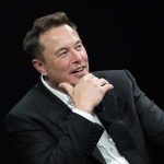 Musk’s $1 Trillion Pay Deal – A Trojan Horse? Man in suit smiling, resting chin on hand.