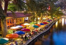 Outdoor riverside restaurant with colorful umbrellas and evening lights.